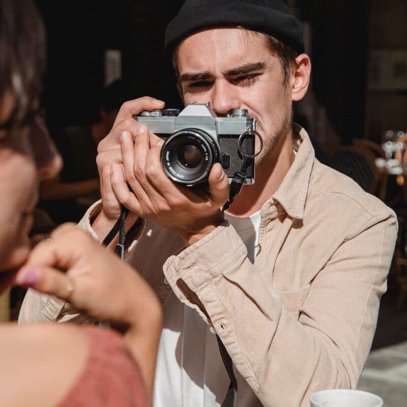 Someone photographing a friend across a cafe table with a film camera