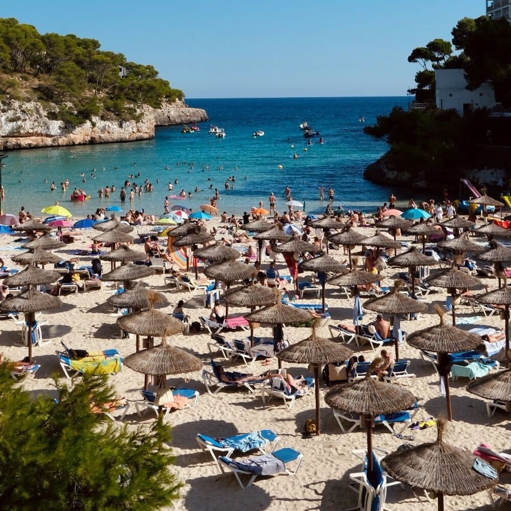 A Mallorcan cove packed with thatched parasols above turquoise water
