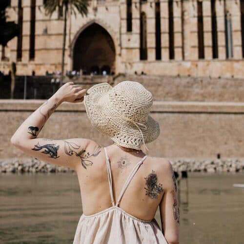 Someone in a straw sun hat facing Palma cathedral across the water